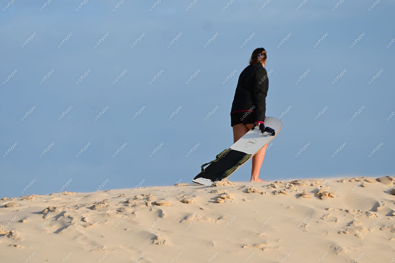Lagoa da Conceição, Florianópolis: Mulher caminhando sobre a duna de areia com prancha de surf