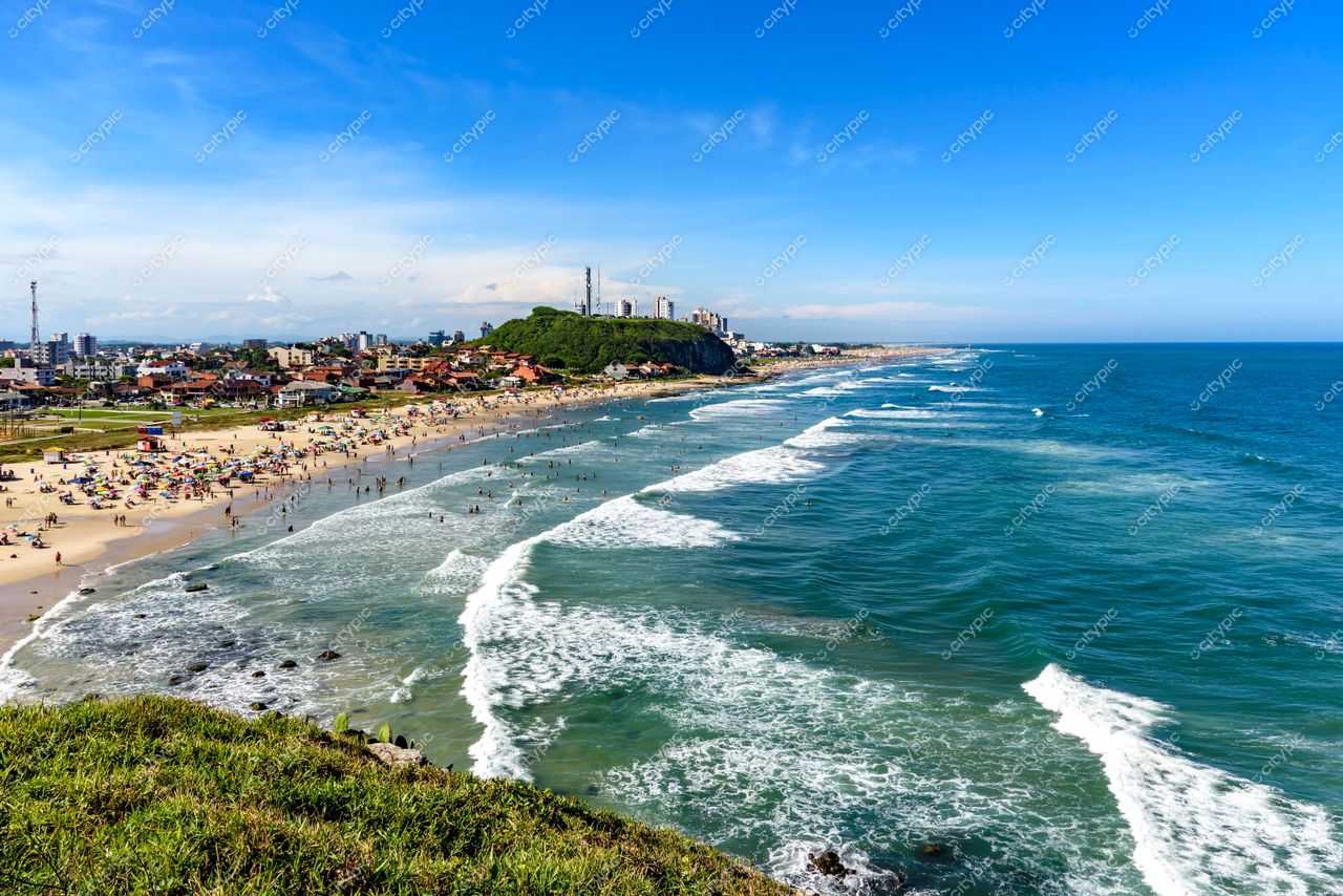 Torres, Rio Grande do Sul: Vista panorâmica da praia com ondas suaves e pessoas desfrutando do dia ensolarado