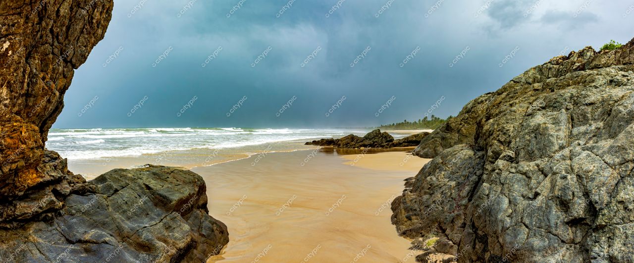 Uruçuca, Bahia: Praia selvagem e dramática com rochas imponentes e nuvens de tempestade no horizonte