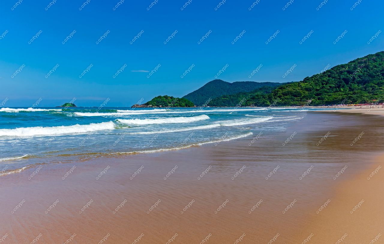 Guarujá, São Paulo: Praia dourada sob o céu azul e montanhas verdejantes ao fundo