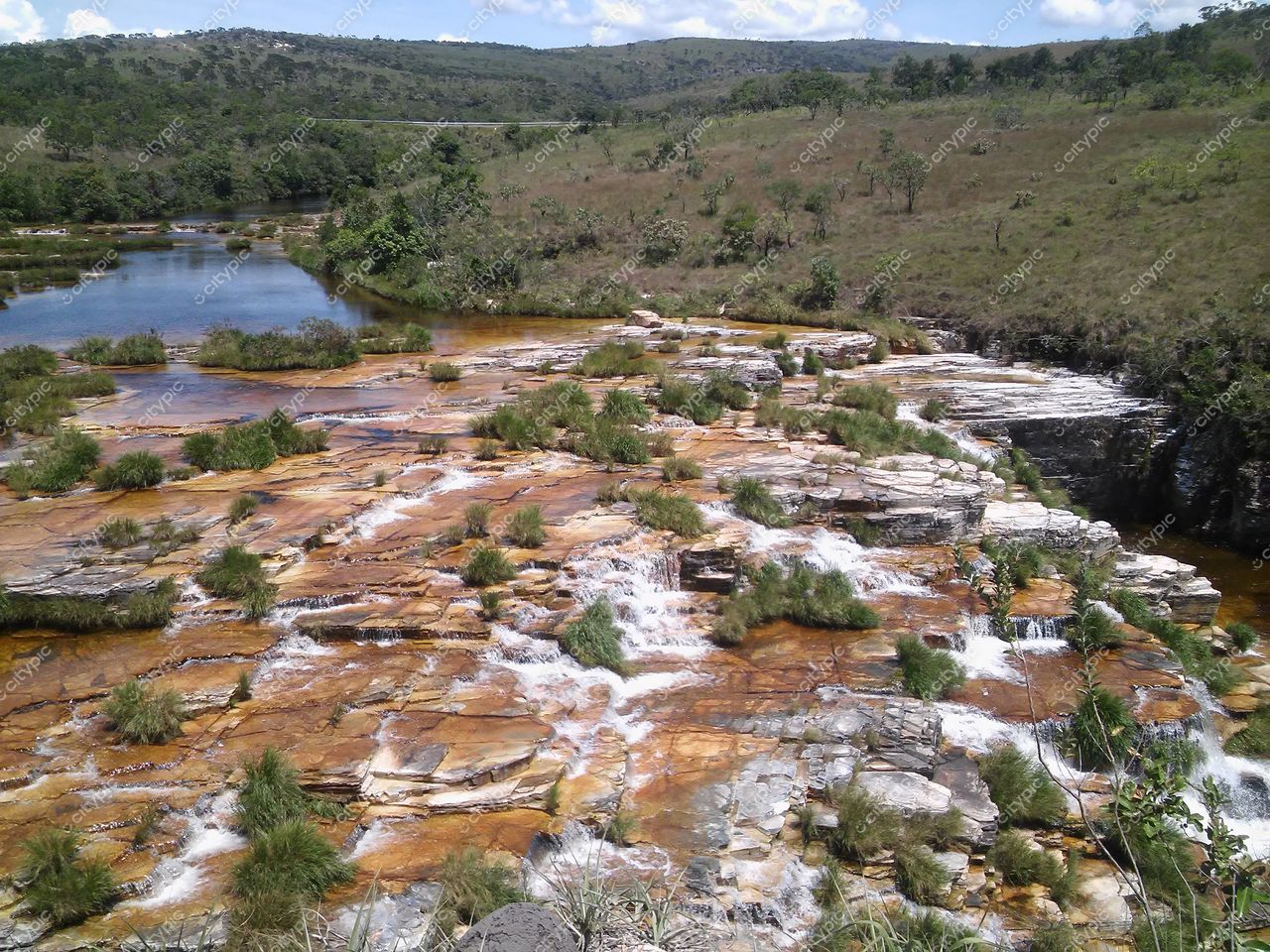 Serra da Canastra, Minas Gerais, leito de rochas alaranjadas com vegetação rasteira e curso d’água em dia claro