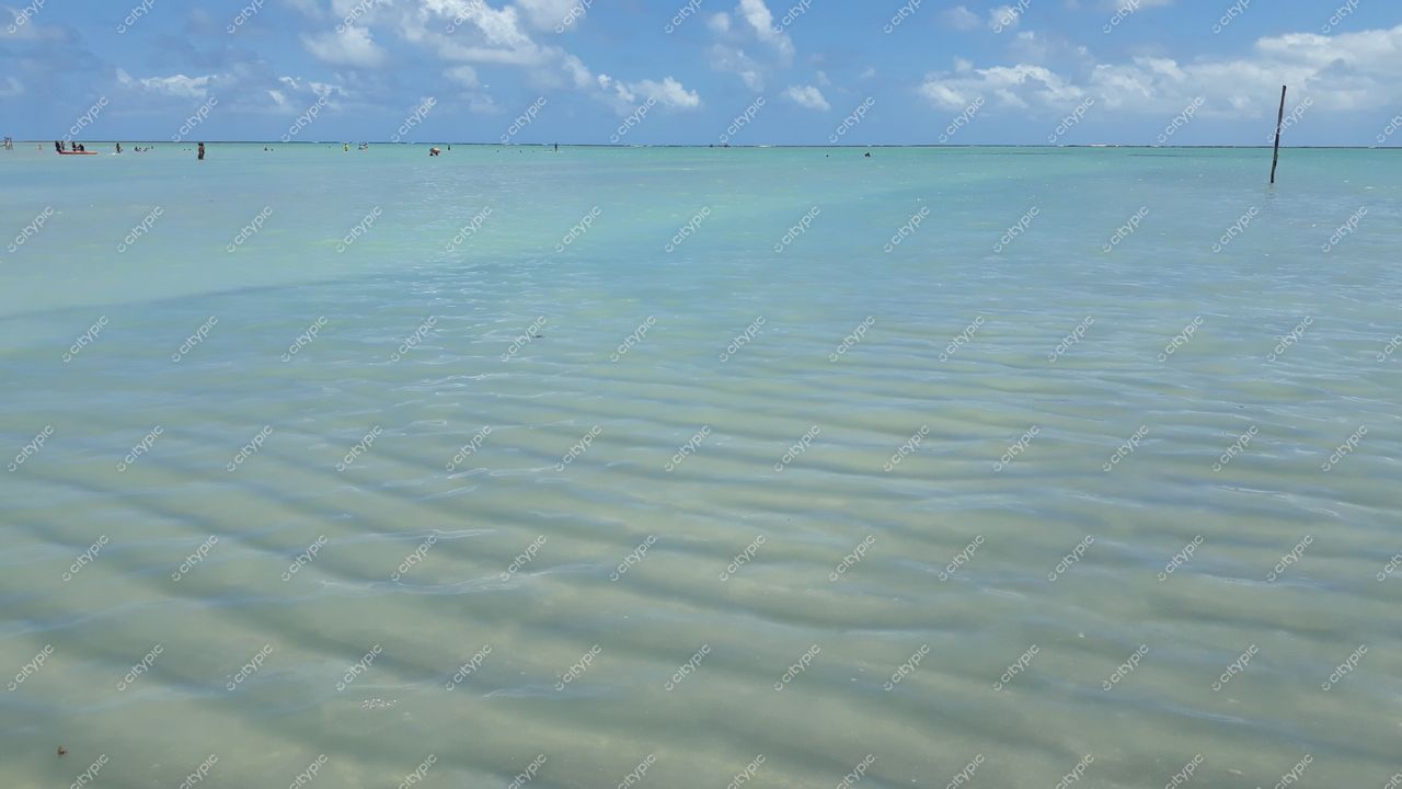 Maragogi, Alagoas com águas rasas e tranquilas refletindo céu nublado e pessoas distantes em ambiente rústico