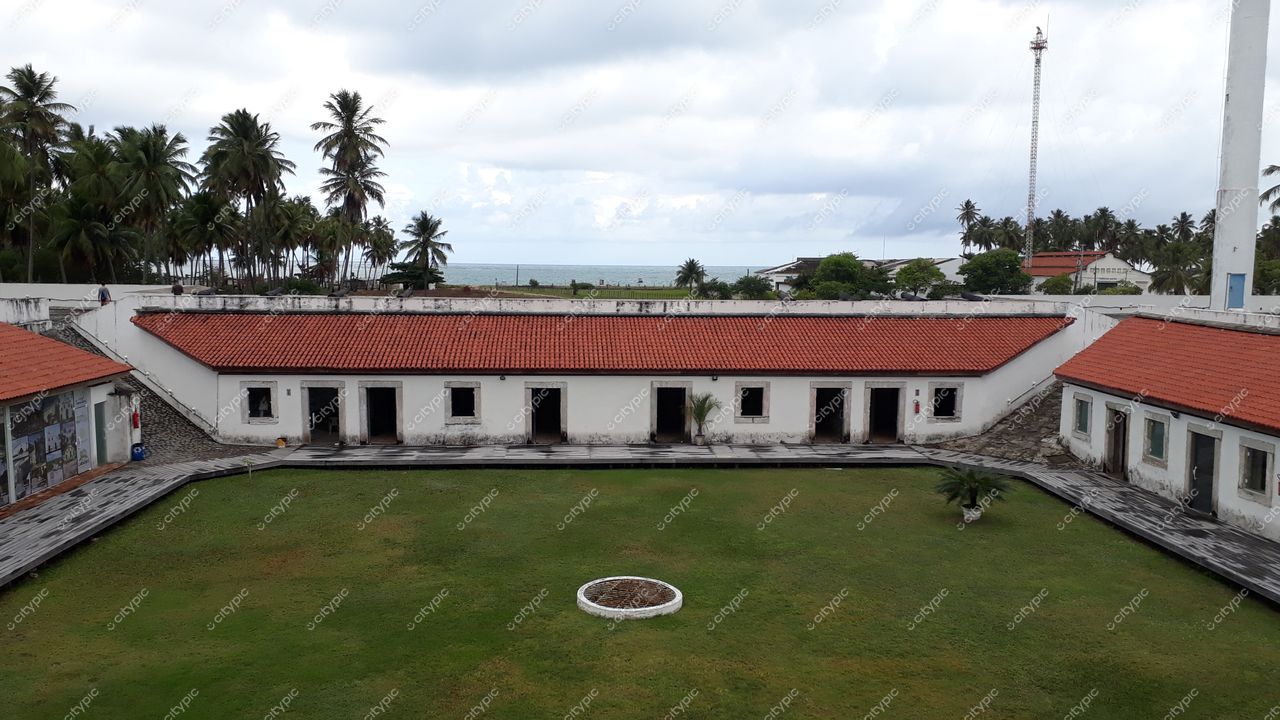 Tamandaré, Pernambuco, vista de gramado cercado por construções brancas e telhados vermelhos sob céu nublado
