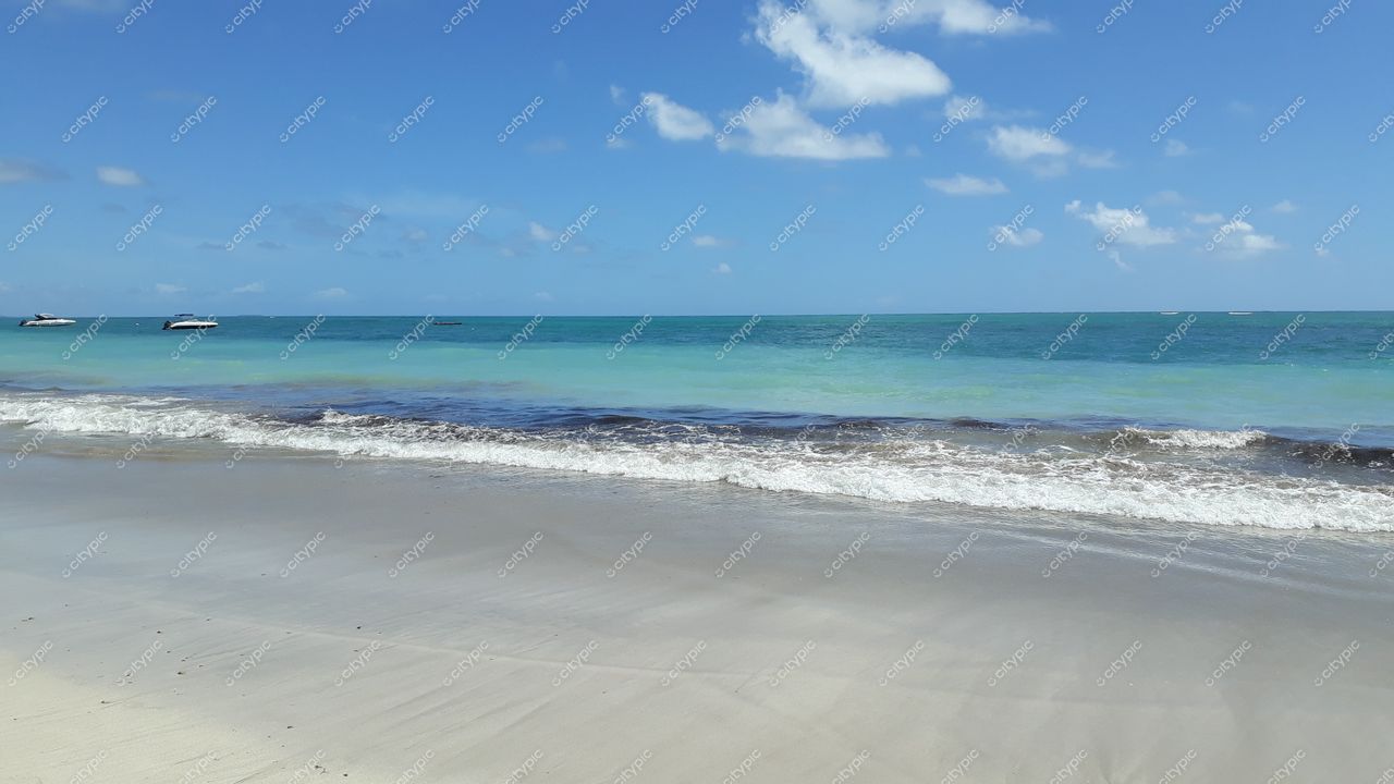 Tamandaré, Pernambuco com praia de areia clara e água em tons de azul sob céu limpo e nuvens dispersas