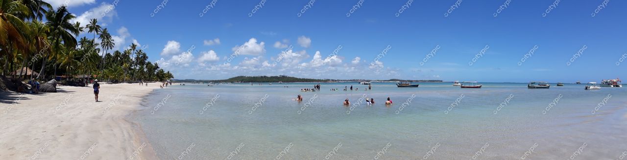 Tamandaré, Pernambuco, praia com águas tranquilas e cristalinas, pessoas na areia clara e embarcações ao fundo