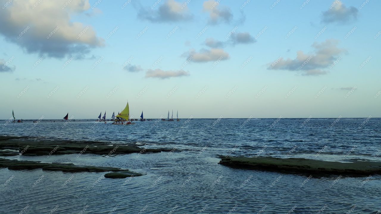 Porto de Galinhas, Pernambuco com barcos a vela coloridos e formações rochosas sob céu nublado ao entardecer