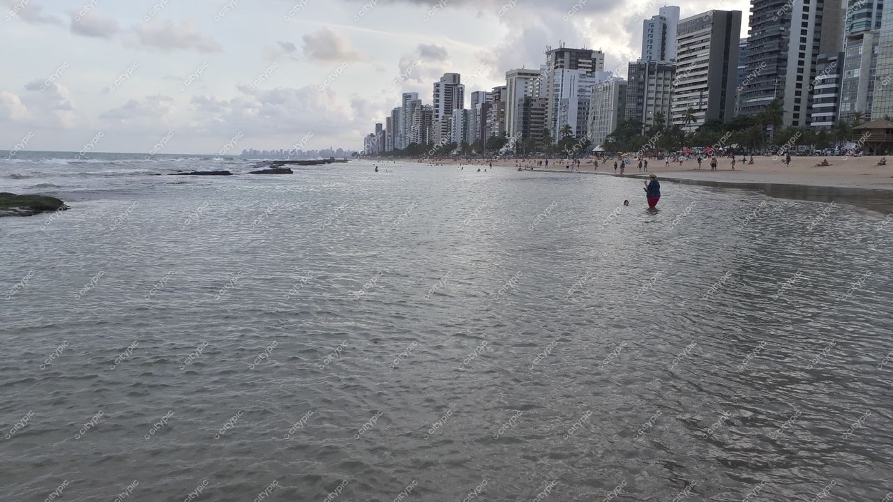 Recife, Pernambuco, praia com arranha-céus ao fundo e pessoas na areia em dia ensolarado de início da tarde