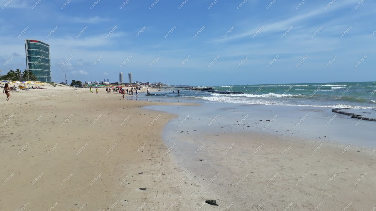 Recife, Pernambuco com praia de areia clara e edifício moderno ao fundo sob céu parcialmente nublado e boa iluminação