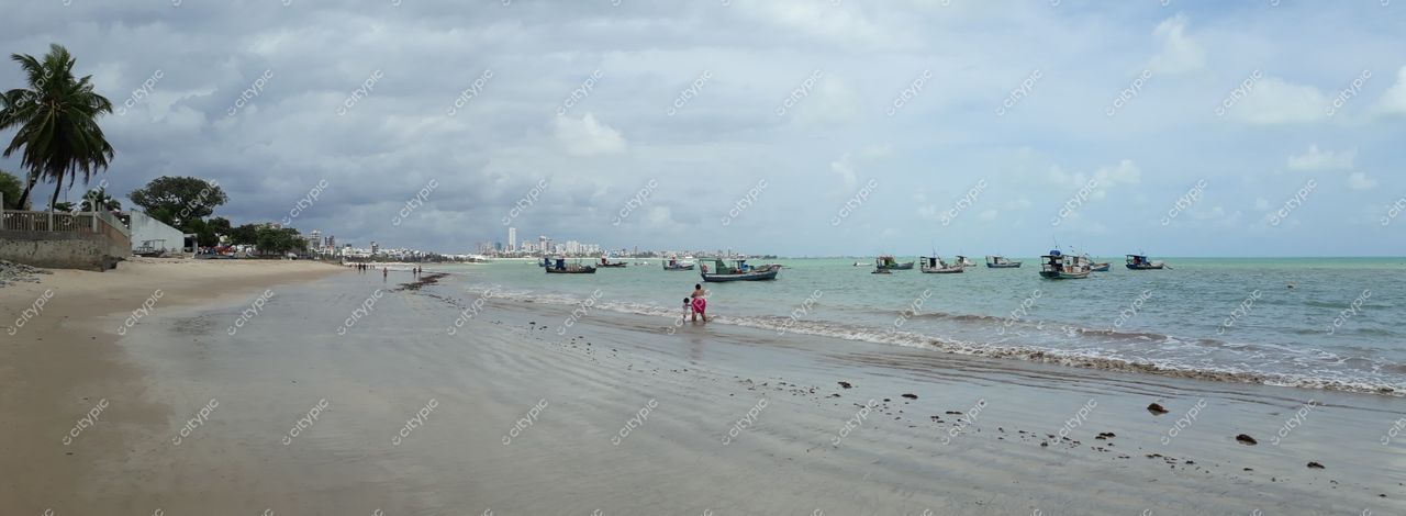 João Pessoa, Paraíba com praia de areia molhada refletindo luz suave em dia nublado e barcos de pesca ao fundo