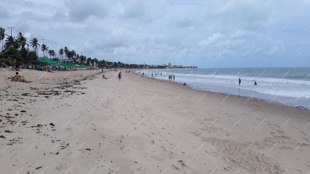 João Pessoa, Paraíba com praia de areias claras e finas sob céu parcialmente nublado e barracas verdes ao fundo