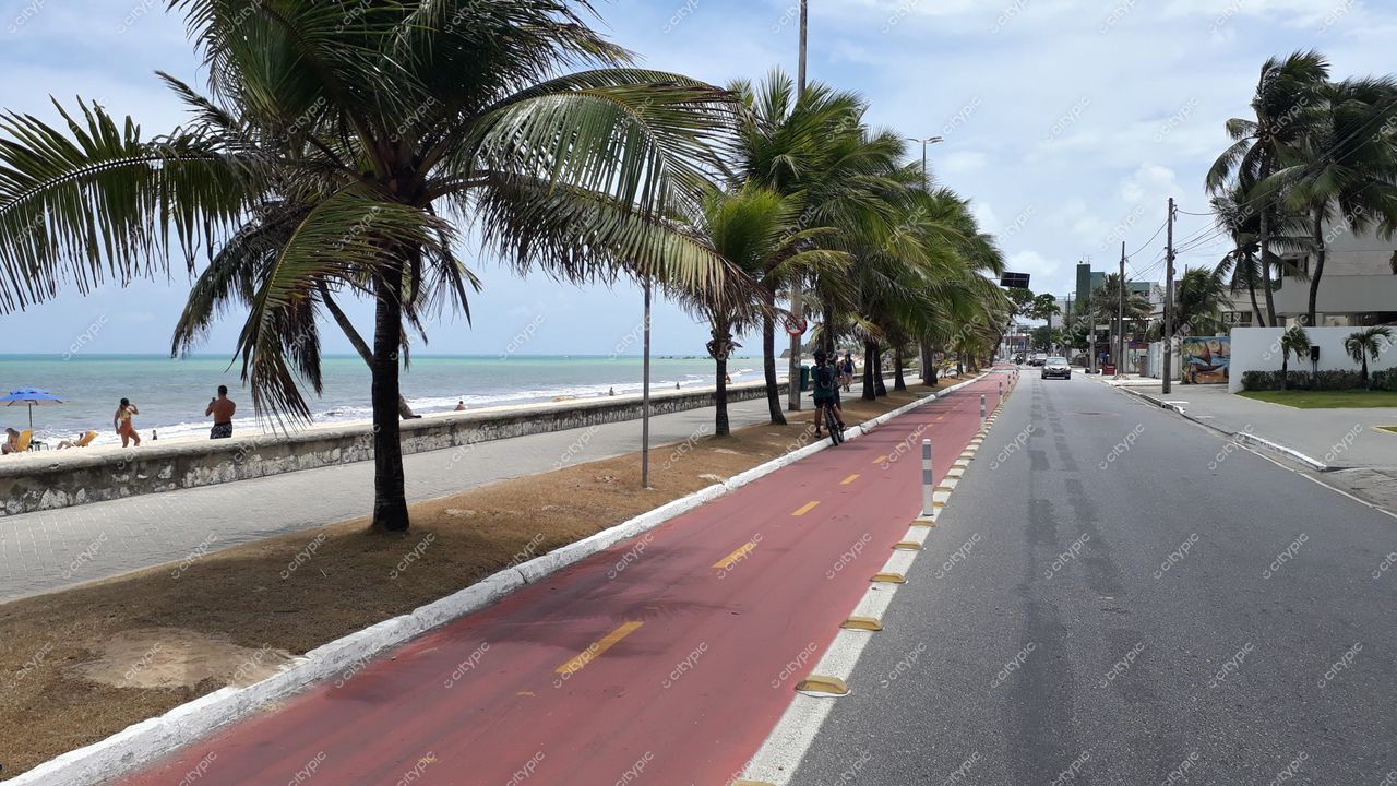 João Pessoa, Paraíba, ciclovia demarcada em vermelho ao lado da praia com pessoas e palmeiras sob céu claro