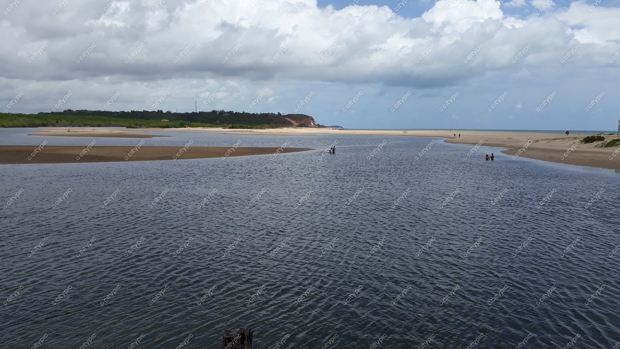 Conde, Paraíba, paisagem ribeirinha com rio de águas escuras, vegetação e colinas sob céu parcialmente nublado