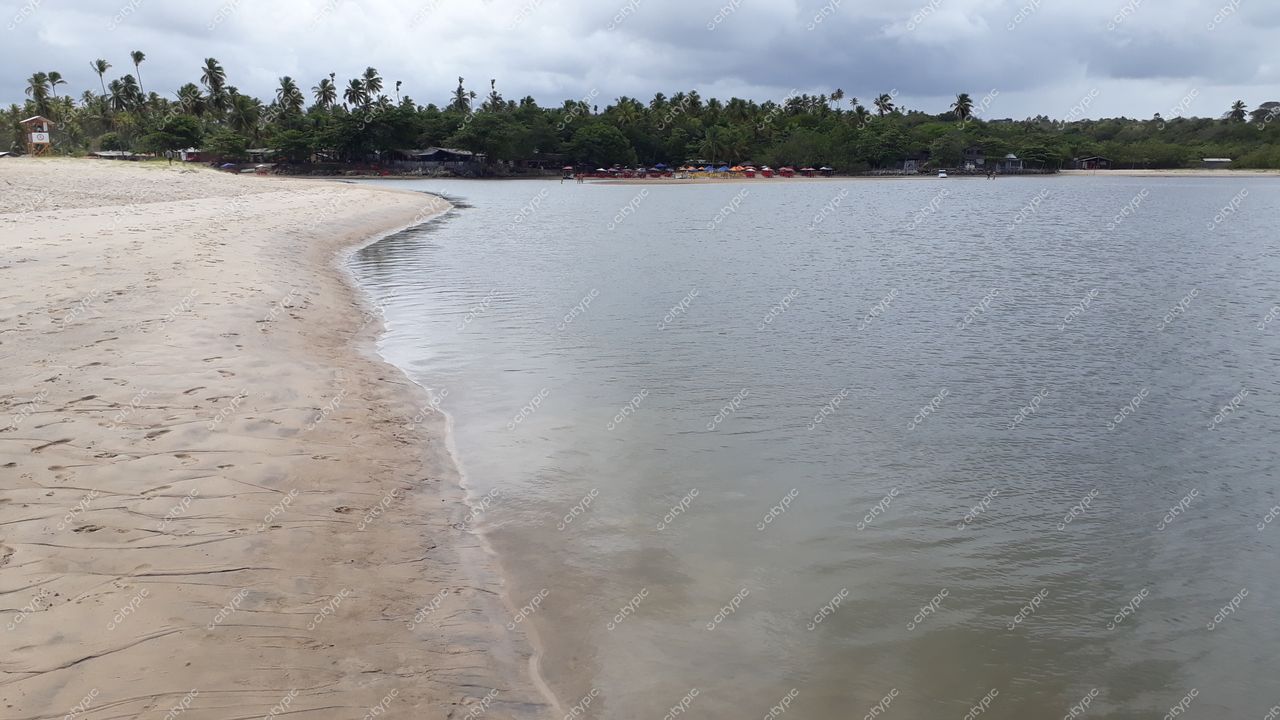 Conde, Paraíba, praia tranquila com areia clara, águas calmas, vegetação densa e construções simples ao fundo