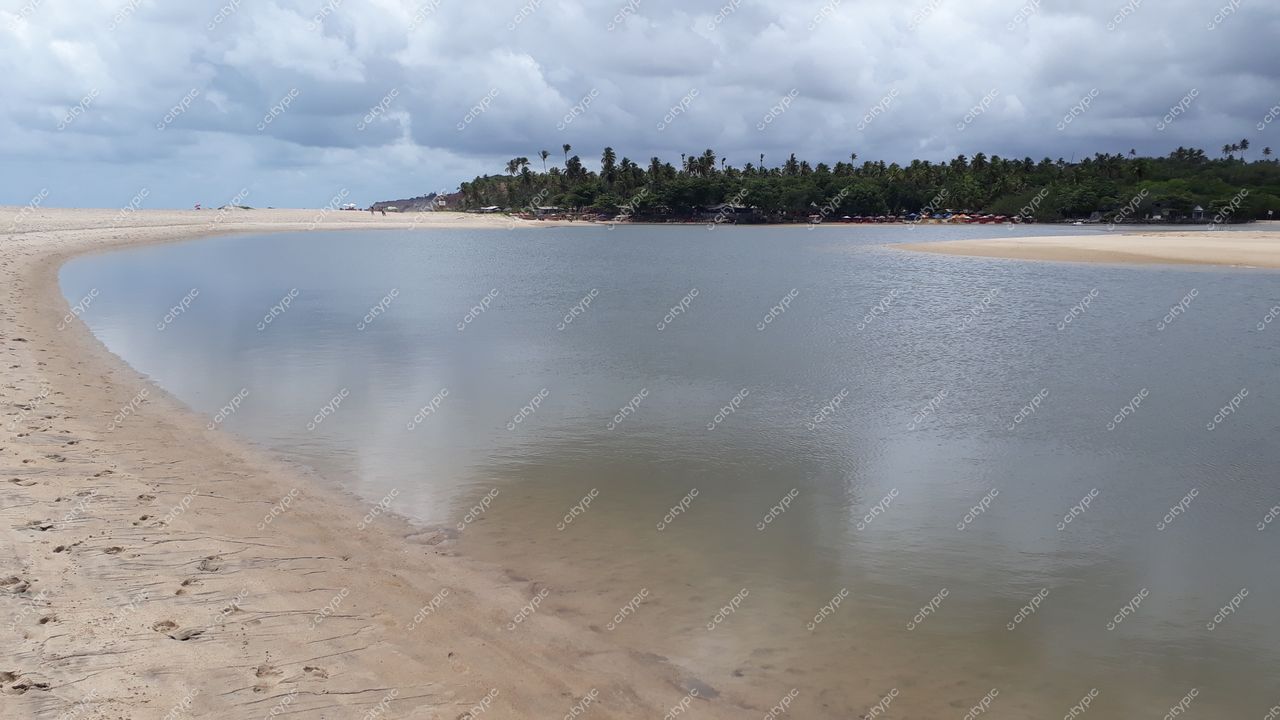 Conde, Paraíba, paisagem tranquila com corpo de água refletindo céu nublado e vegetação exuberante ao fundo