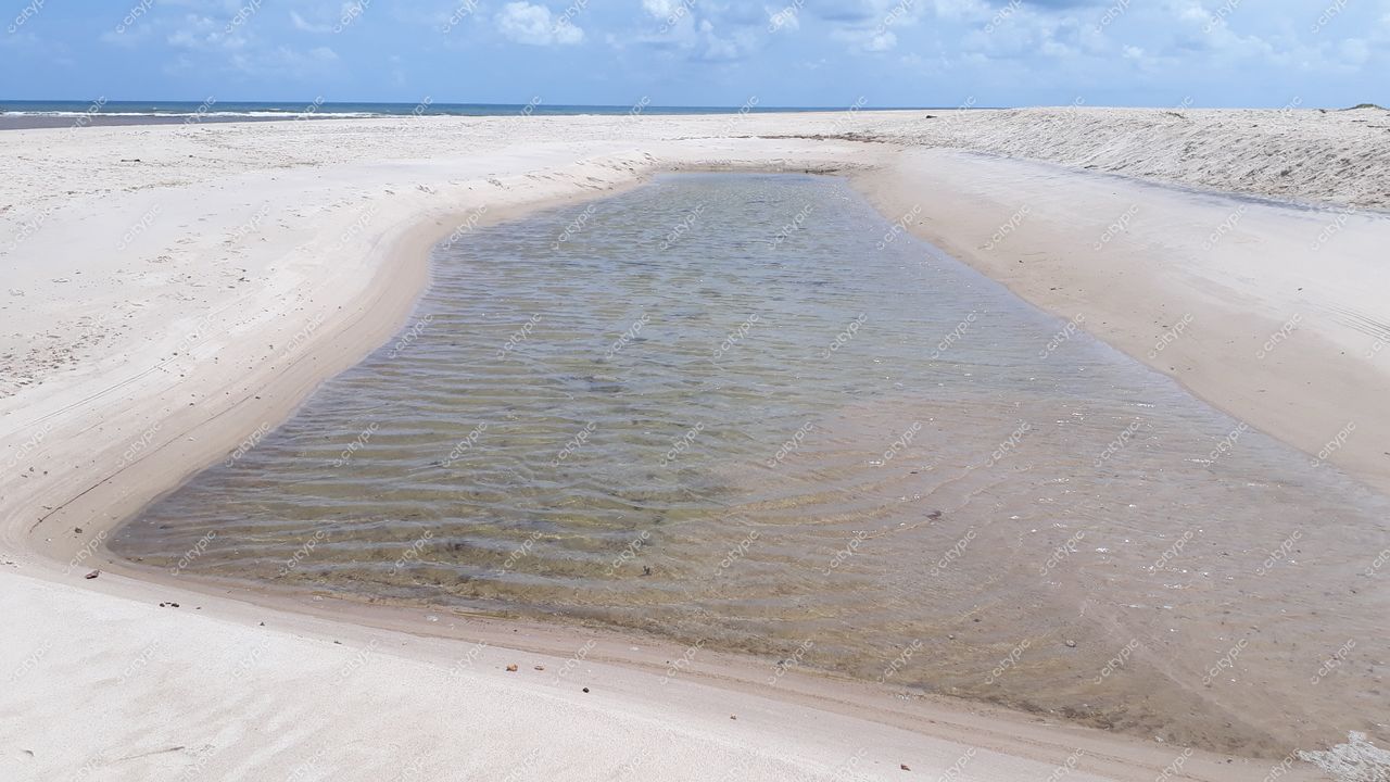 Conde, Paraíba Lagoa rasa em praia arenosa com céu claro e nuvens dispersas ao fundo e ondas suaves