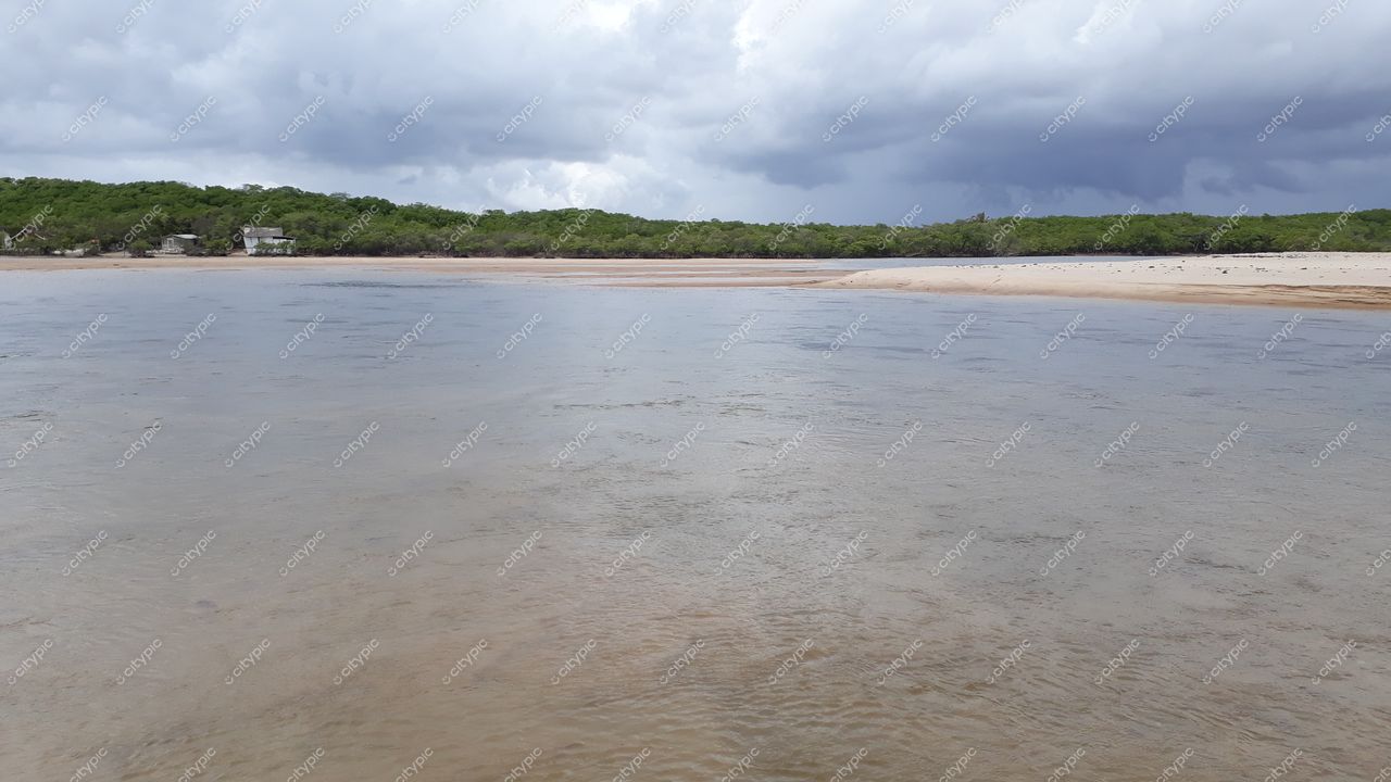 Conde, Paraíba, paisagem tranquila com água rasa e areia na margem sob céu nublado e vegetação rasteira