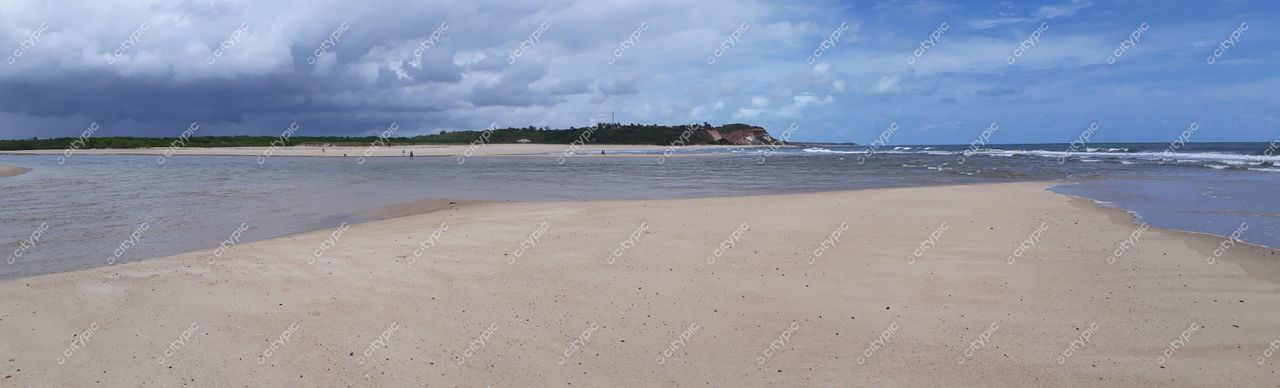 Conde, Paraíba, praia tranquila com areia clara e mar calmo sob céu parcialmente nublado e vegetação rasteira
