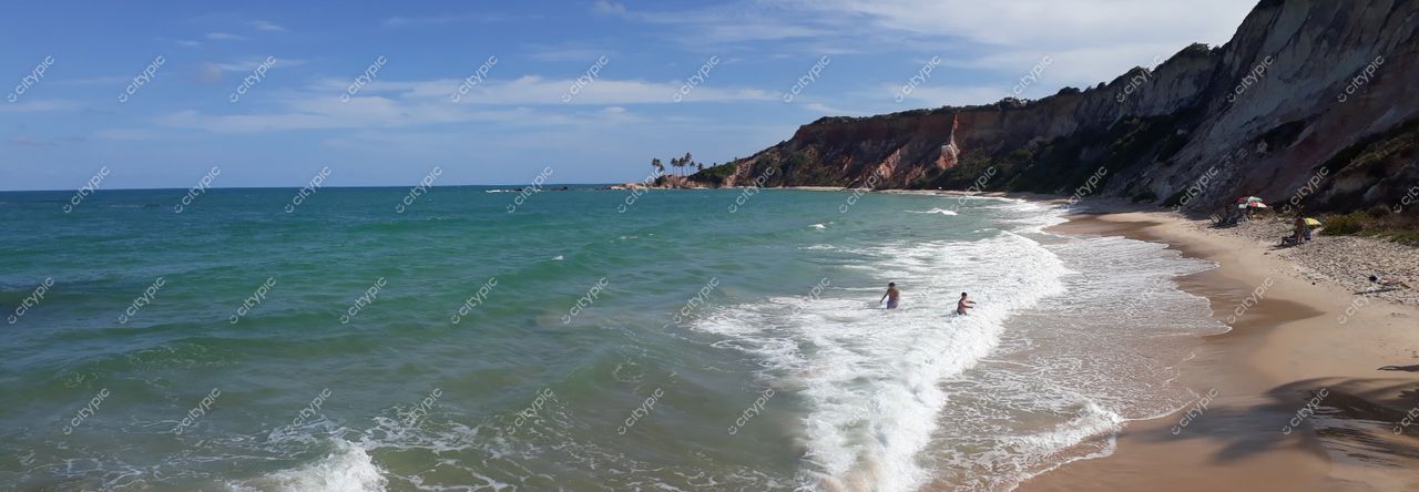 Conde, Paraíba, praia com areia clara e fina, águas azul-esverdeadas e falésias ao fundo em dia ensolarado