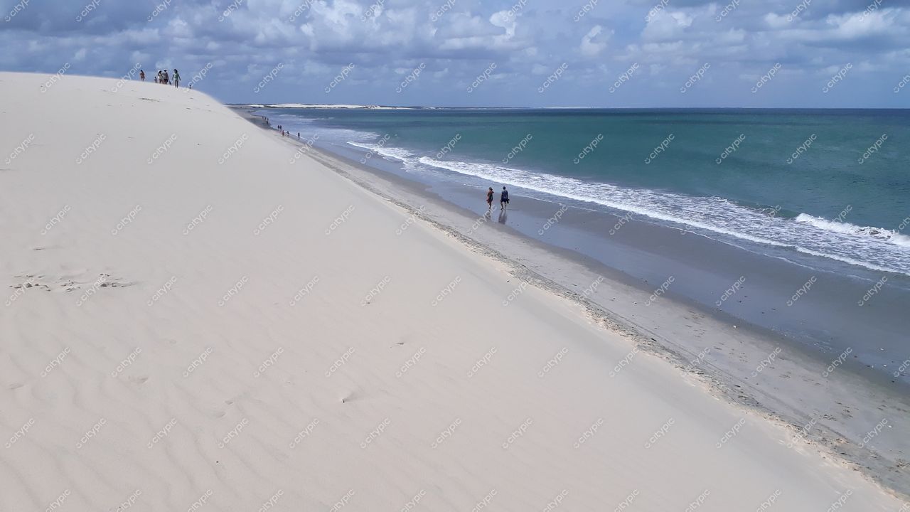 Jijoca de Jericoacoara, Ceará vista da praia com duna clara e pessoas caminhando sob céu parcialmente nublado