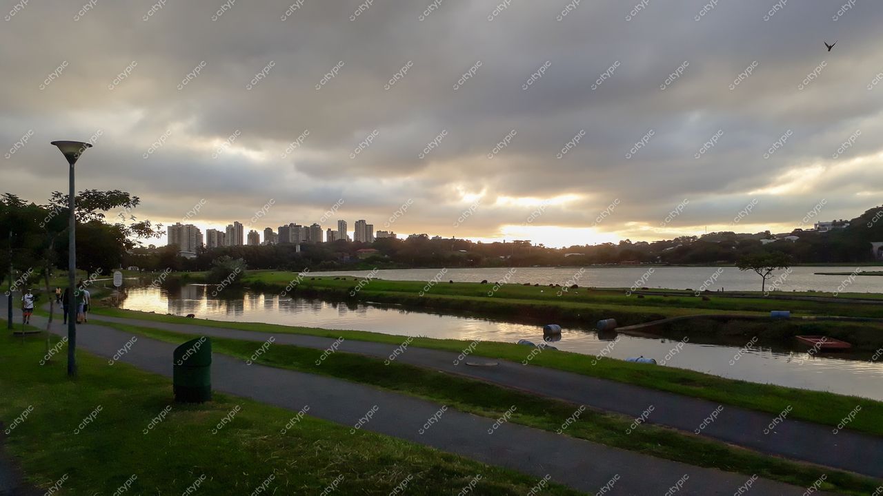 Curitiba, Paraná, parque à beira do lago com ciclovia e pessoas caminhando sob céu nublado ao entardecer