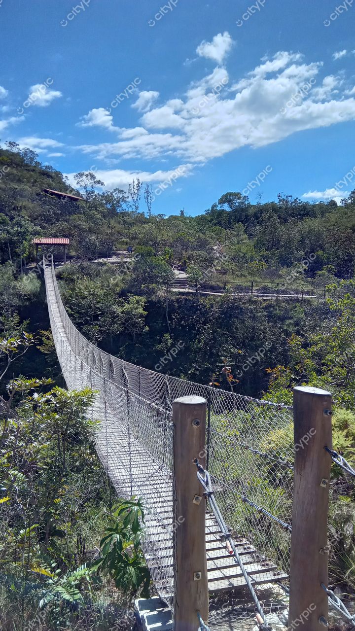 Pirenópolis, Goiás, ponte suspensa em dia ensolarado com vegetação densa e montanhas ao fundo