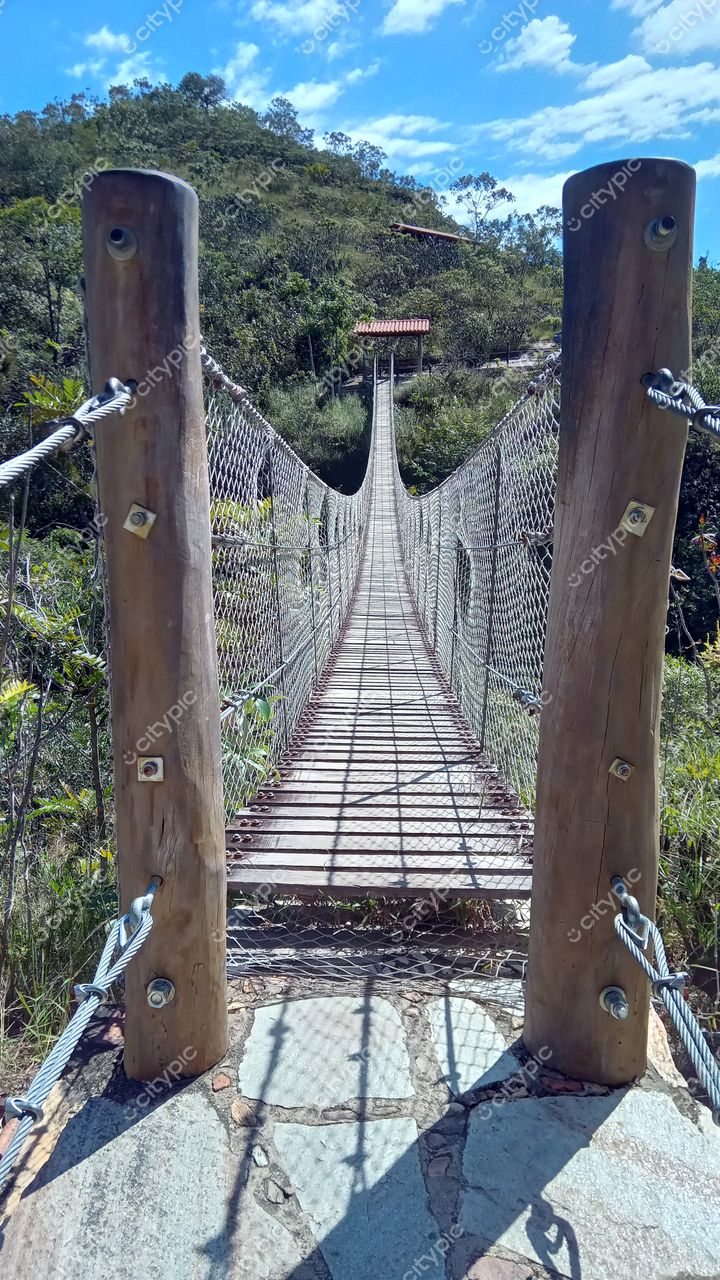 Pirenópolis, Goiás, ponte suspensa de madeira e cabos de aço em dia ensolarado com vegetação densa ao fundo