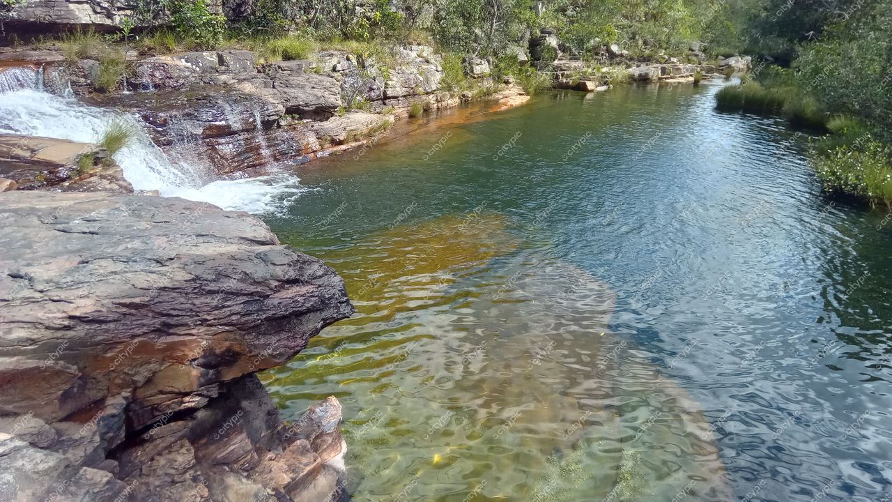 Chapada dos Veadeiros, Goiás, formação rochosa com cachoeira e lago de água clara em vegetação densa e iluminação suave