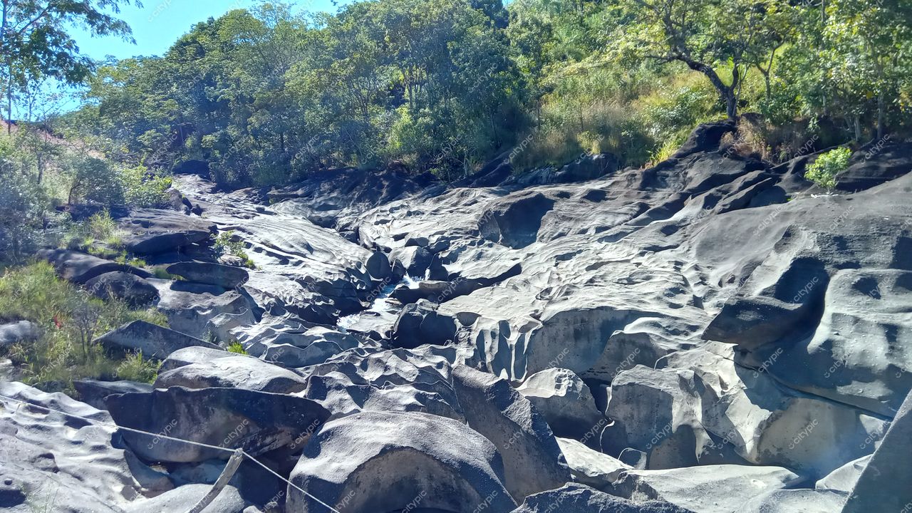 Chapada dos Veadeiros, Goiás, rochas escuras e irregulares cercadas por vegetação nativa sob luz do dia clara