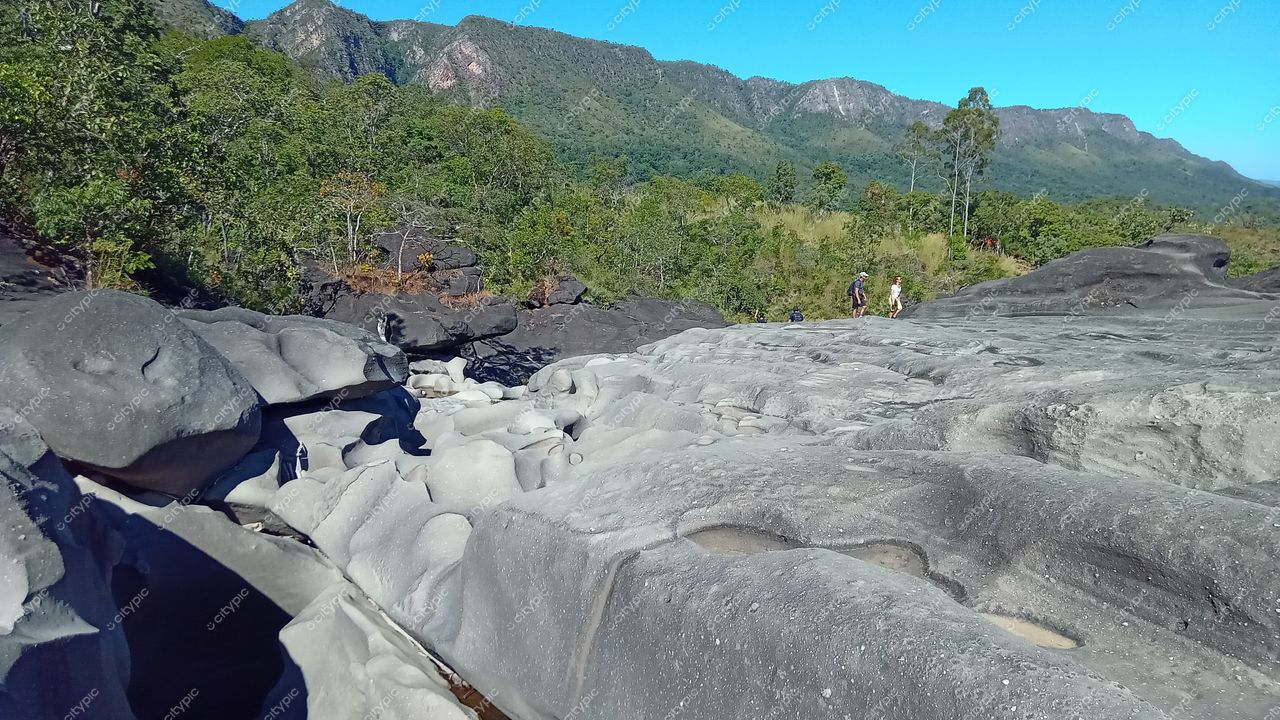 Chapada dos Veadeiros, Goiás, rochas esculpidas em tons claros e escuros com vegetação exuberante e pessoas caminhando ao sol