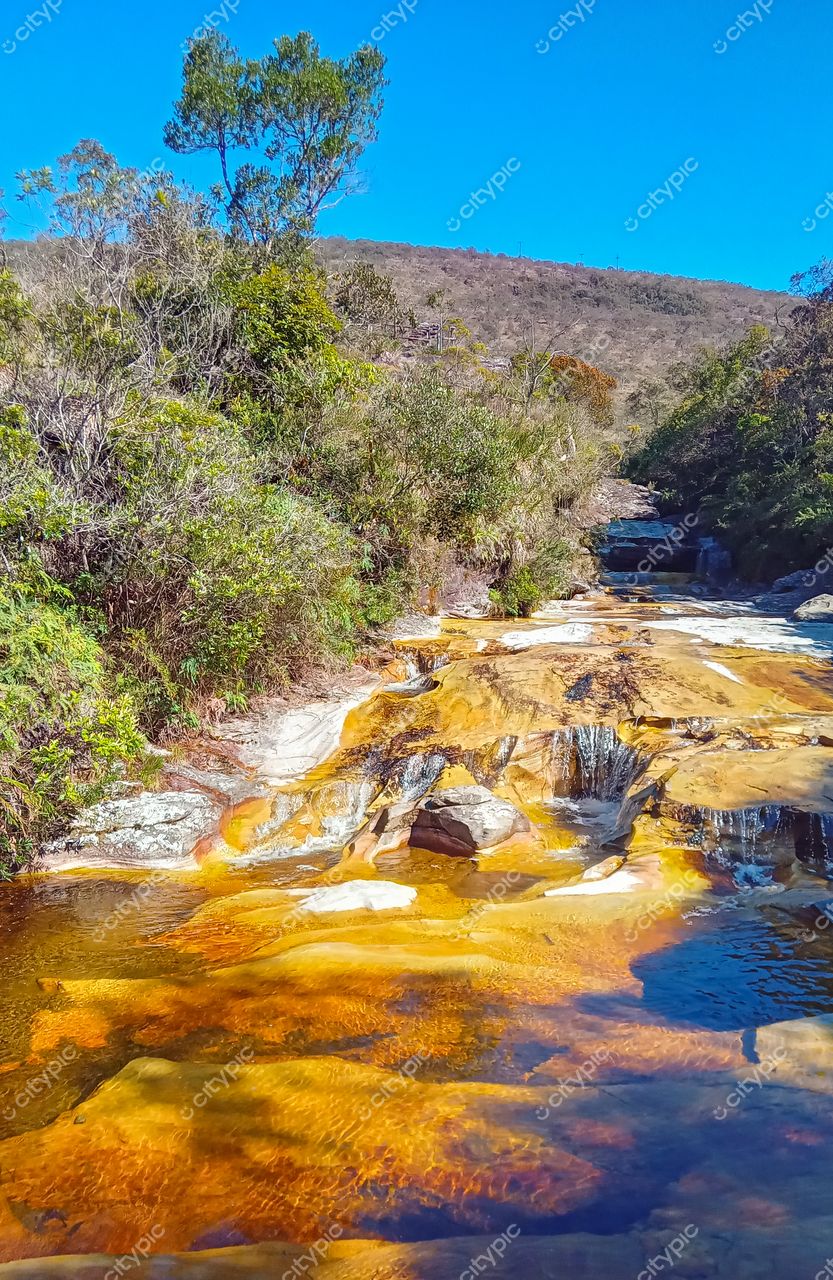 Ibitipoca, Minas Gerais, leito de água cristalina entre pedras laranja e amarelo sob céu azul sem nuvens