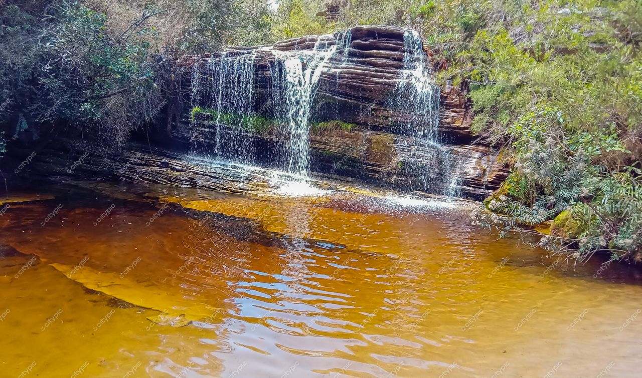 Ibitipoca, Minas Gerais, cachoeira com água cristalina e lago alaranjado cercado por vegetação densa em iluminação suave