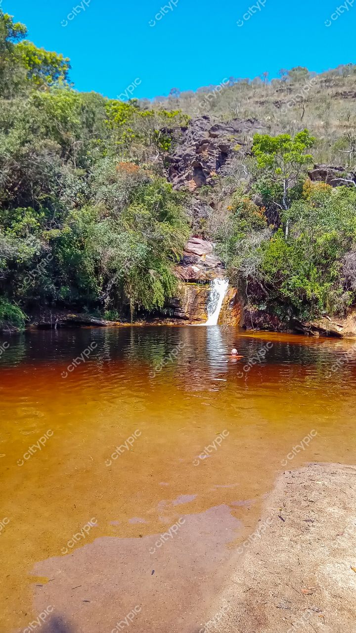 Ibitipoca, Minas Gerais, cachoeira com poço âmbar e vegetação exuberante em dia ensolarado e céu azul claro
