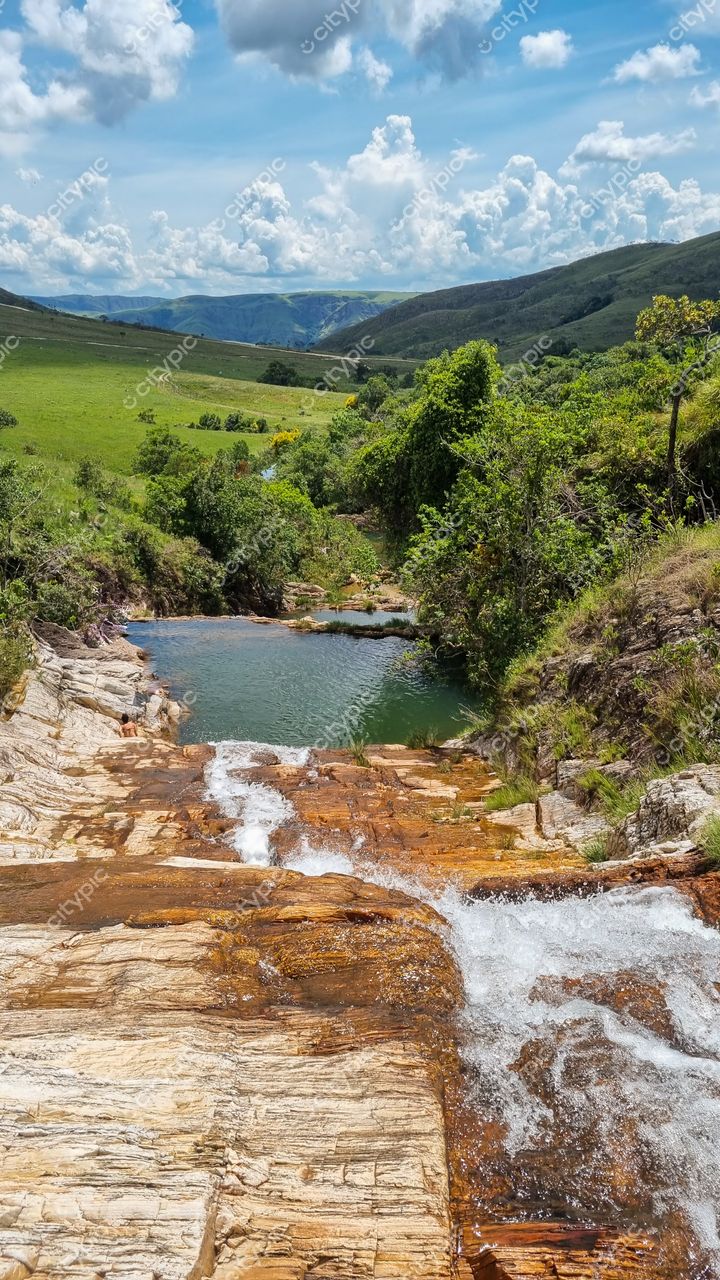Serra da Canastra, Minas Gerais com cascata de águas cristalinas e vegetação exuberante sob céu azul e nuvens brancas