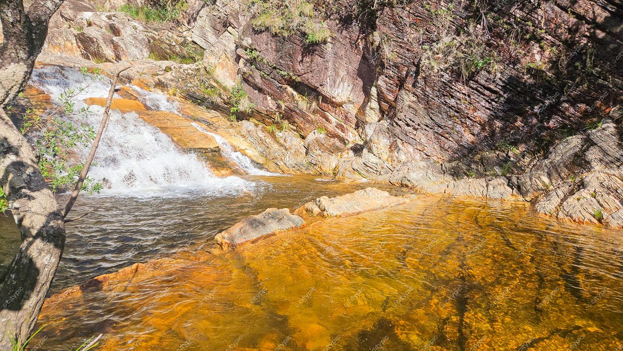 Serra da Canastra, Minas Gerais, queda d’água em poço alaranjado com formações rochosas e vegetação ao fundo