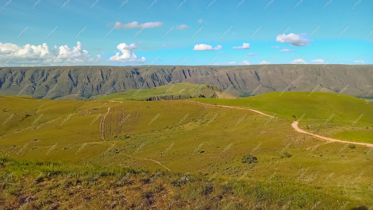 Serra da Canastra, Minas Gerais, vista panorâmica com colinas verdes e caminho de terra sob céu claro e nuvens