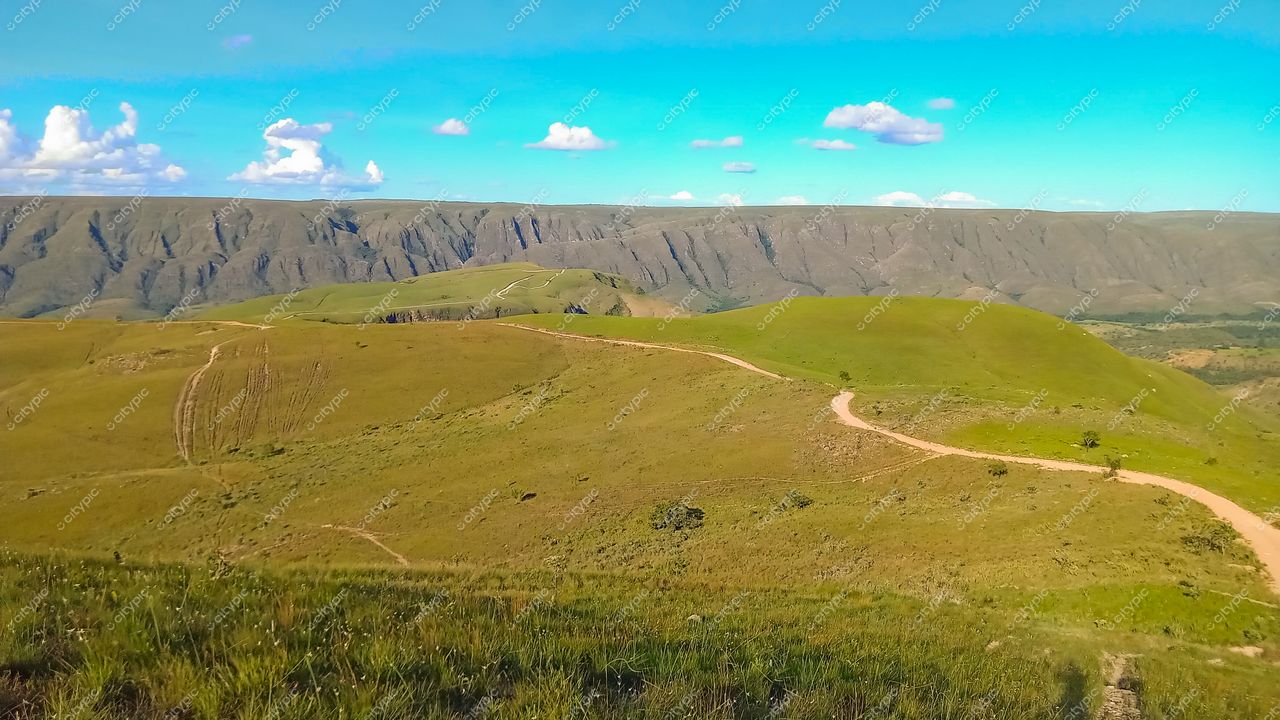 Serra da Canastra, Minas Gerais com colinas verdes e caminho de terra sob céu azul e nuvens esparsas
