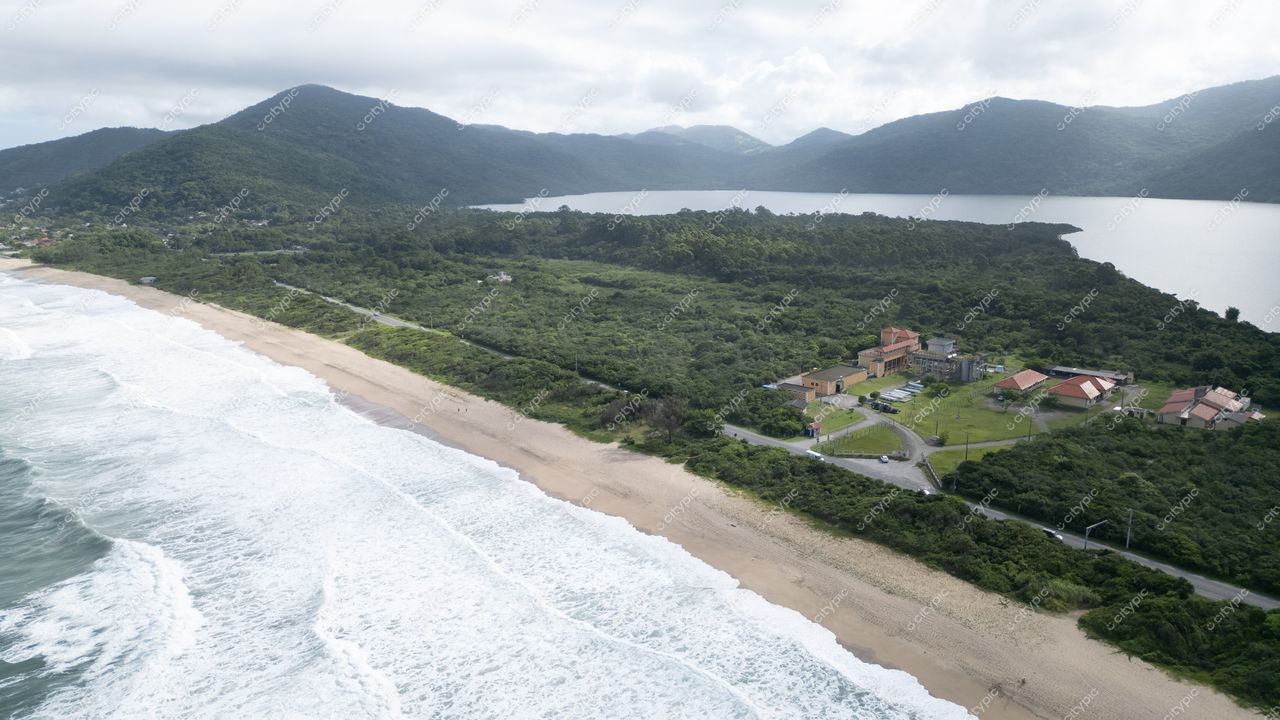 Morro das Pedras e Lagoa do Peri em Florianópolis com praia, vegetação densa e construções sob céu nublado
