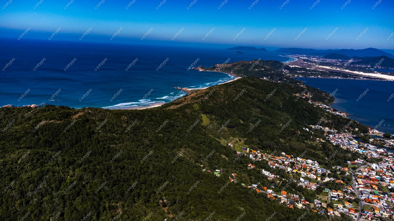 Barra da Lagoa em Florianópolis com vista aérea de montanhas verdes, praia clara e casas coloridas sob céu ensolarado