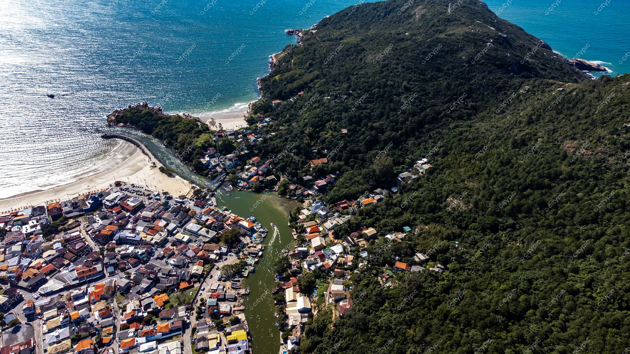 Barra da Lagoa em Florianópolis com vista aérea de casas coloridas, canal e colina verde em dia ensolarado