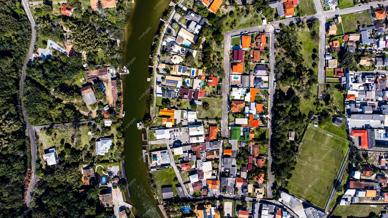 Barra da Lagoa em Florianópolis com casas coloridas, áreas verdes e um campo de futebol em dia ensolarado