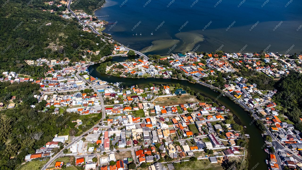 Barra da Lagoa em Florianópolis com vista aérea de casas coloridas, vegetação densa e água tranquila em dia ensolarado