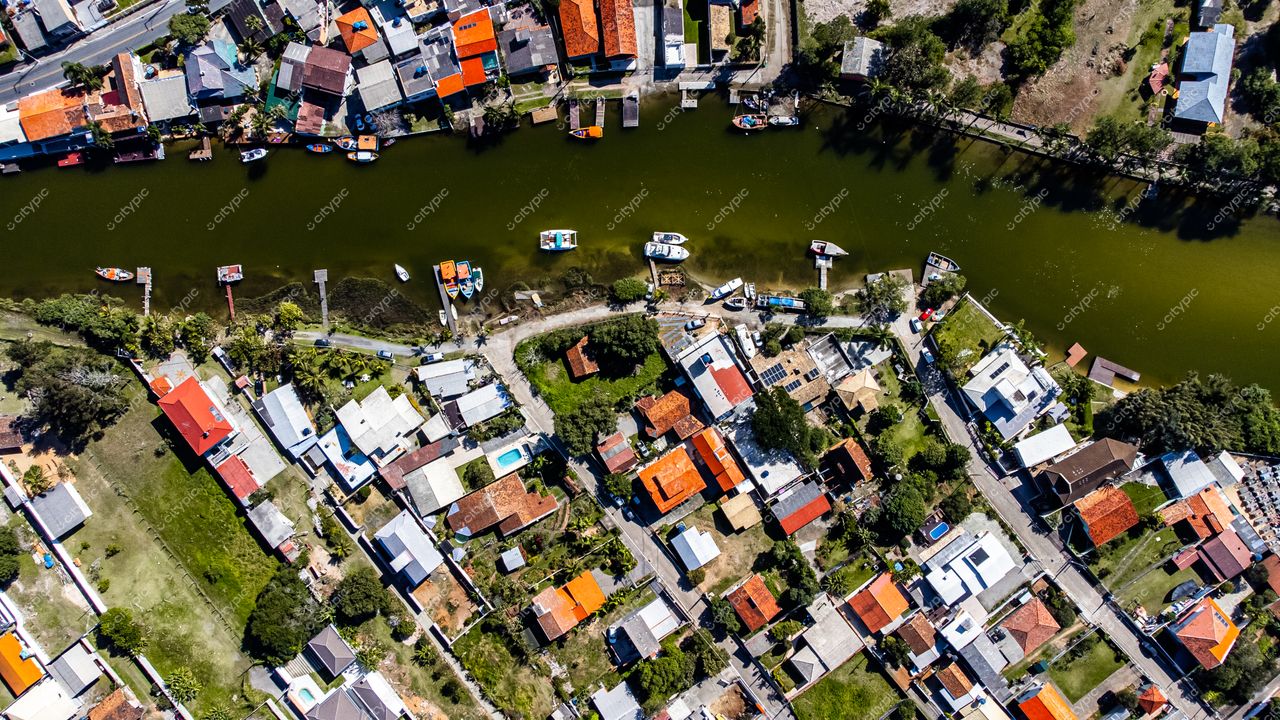 Barra da Lagoa em Florianópolis com casas coloridas, vegetação abundante e barcos ancorados em dia ensolarado