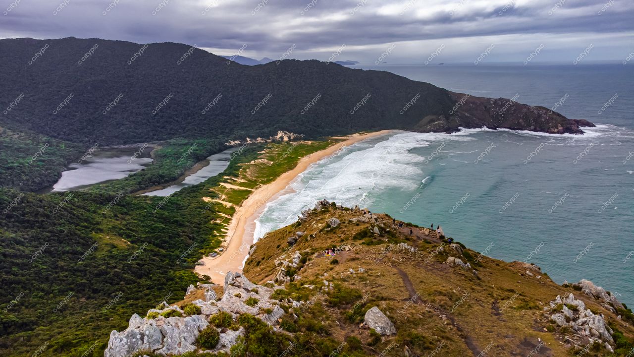 Lagoinha do Leste em Florianópolis com montanhas arborizadas e praia dourada sob iluminação nublada e pessoas contemplando a vista