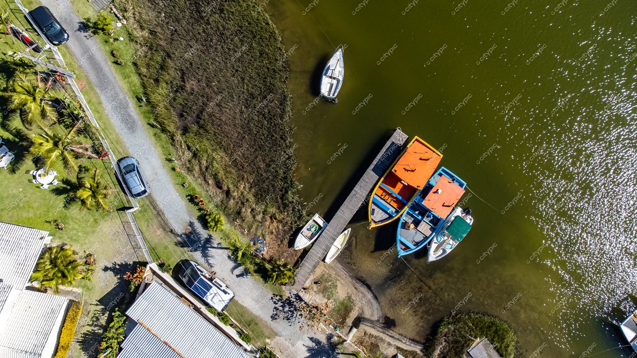 Barra da Lagoa em Florianópolis com embarcações coloridas ancoradas, casas brancas e estrada de cascalho à beira-mar
