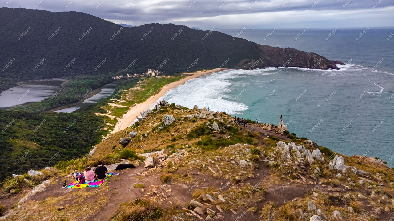 Lagoinha do Leste em Florianópolis com pessoas sentadas em local elevado em dia nublado e vegetação densa ao fundo
