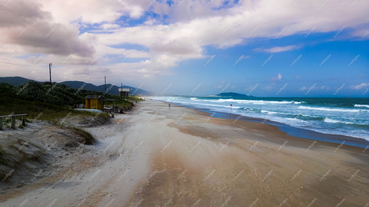 Campeche em Florianópolis com faixa de areia clara, montanhas ao fundo e quiosques na costa durante o dia