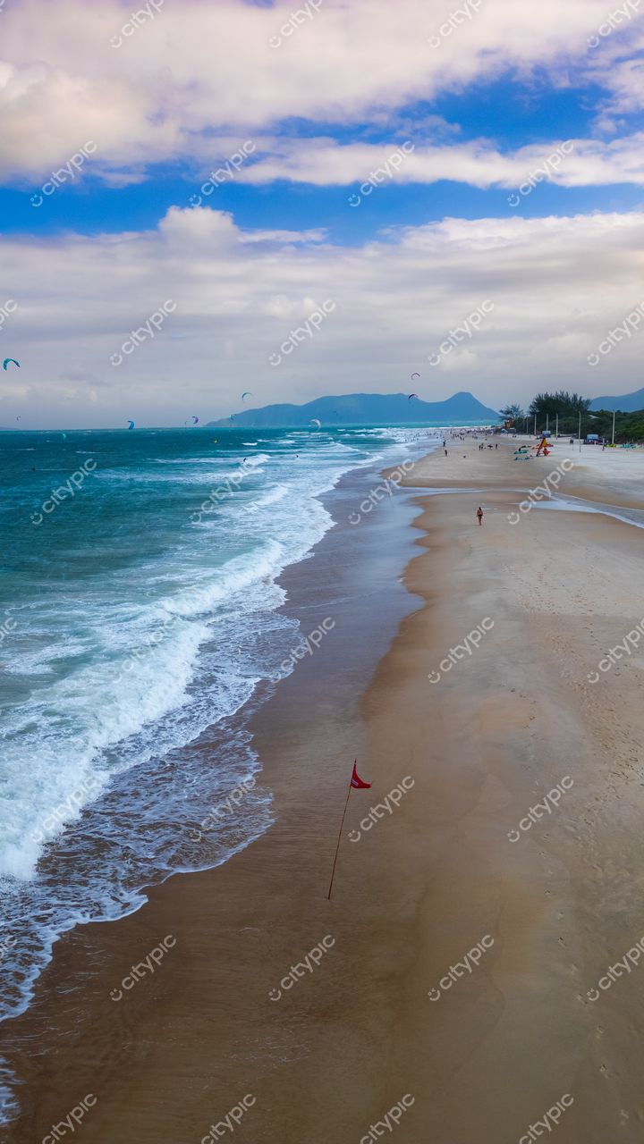 Campeche em Florianópolis com céu azul claro, kitesurfistas ao longe e edificações urbanas ao fundo