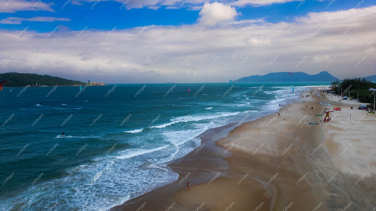 Campeche em Florianópolis com faixa de areia dourada, águas azuladas e vegetação ao fundo em dia parcialmente nublado