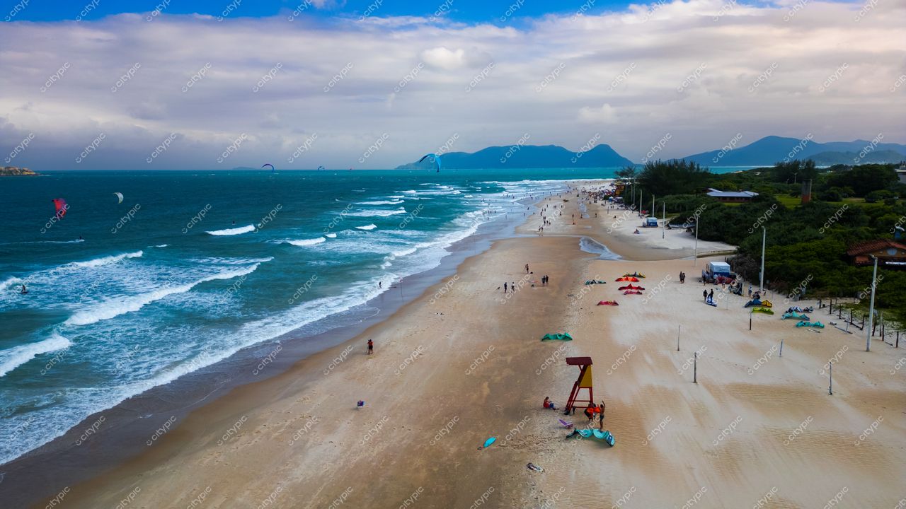 Campeche em Florianópolis com dia nublado, praticantes de kitesurf e quiosques coloridos na areia clara