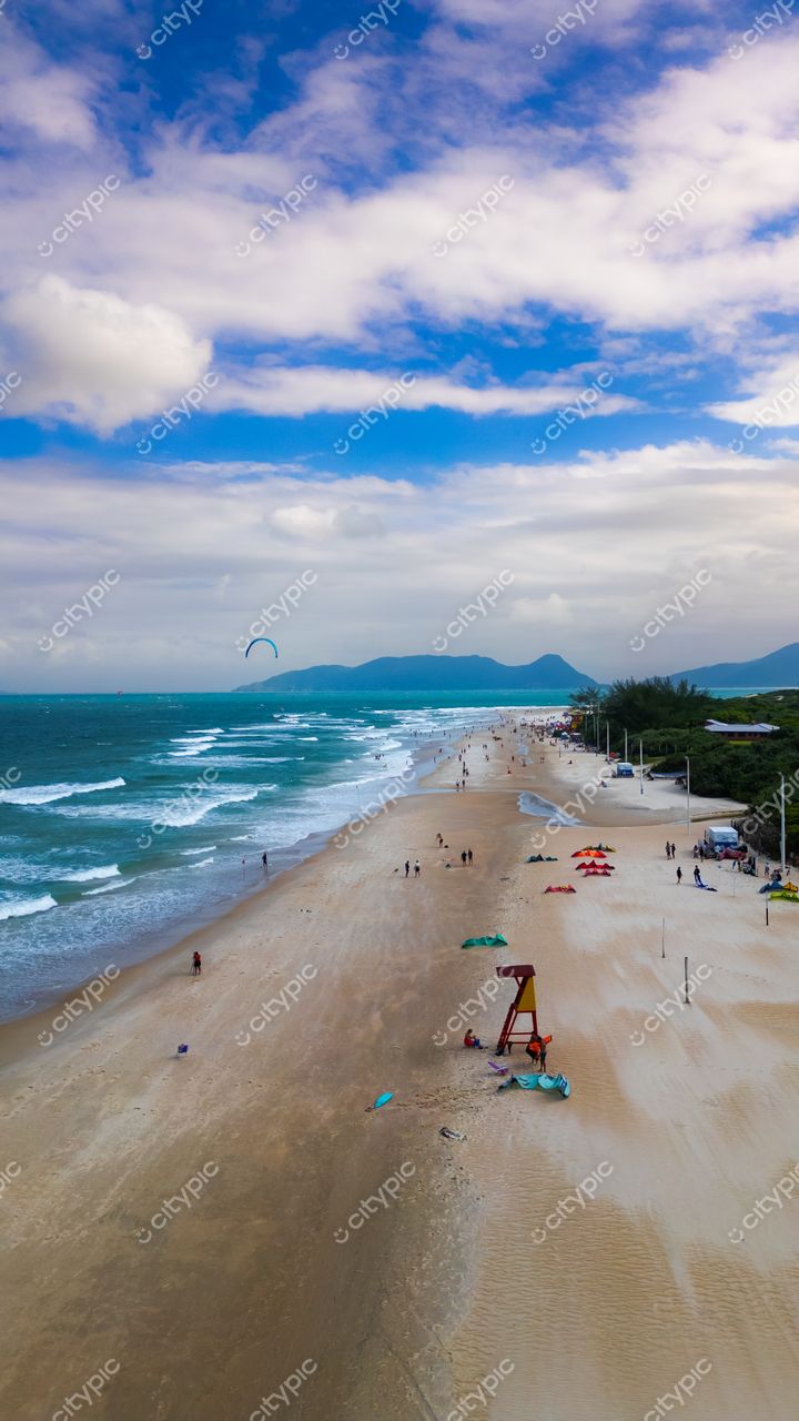 Campeche em Florianópolis com ondas suaves, céu parcialmente nublado e banhistas na areia em dia claro